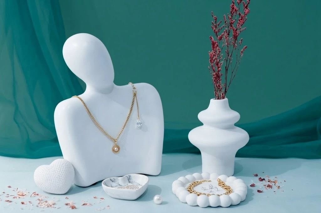 Collar dorado con perla y pulsera de eslabones sobre figuras blancas, con fondo turquesa y flores secas